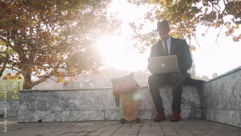 Hipster businessman working on his laptop outside in the park at autumn day Hipster businessman working on his laptop outside in the park at autumn day