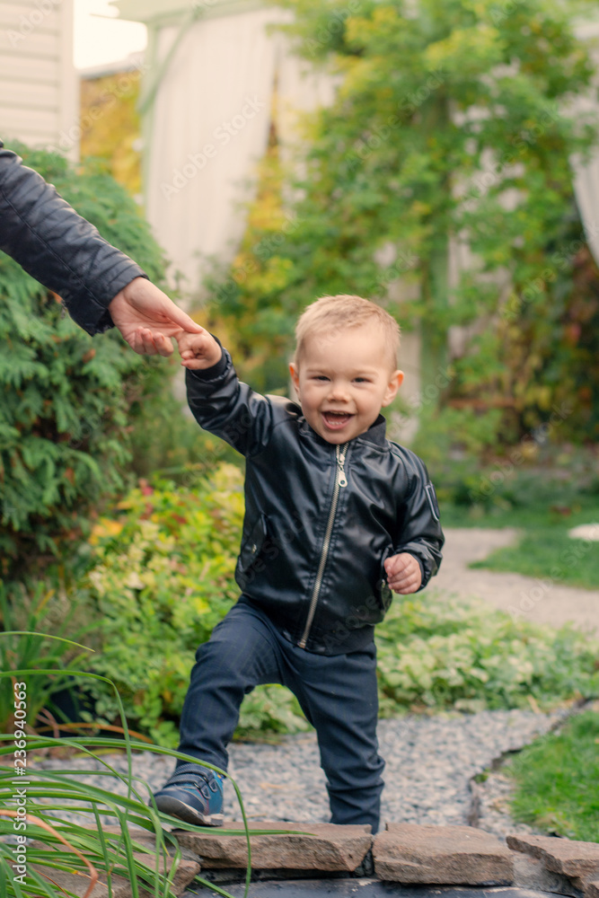 A little boy in the park holds up a hand. A child learns to walk. Fashionable boy laughs A little boy in the park holds up a hand. A child learns to walk. Fashionable boy laughs