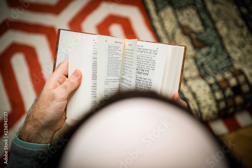Reading book view from above of Jewish male wearing Kippah praying reading Bi-lingual Hebrew French mahzor prayer book from 1920 used on the High Holy Days of Rosh Hashanah and Yom Kippur.