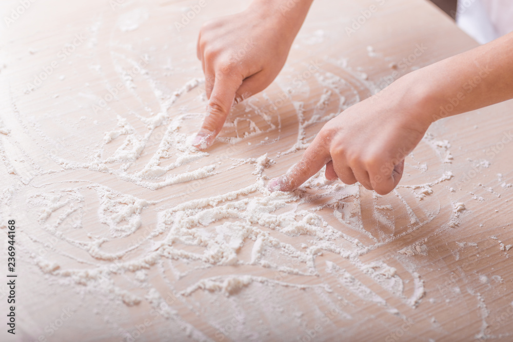 children's hands draw patterns of white flour on the table. baking preparation stage. little game children's hands draw patterns of white flour on the table. baking preparation stage. little game