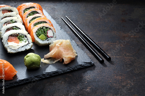 Sushi, rolki na ciemnym tle. Apetyczne, różnorodne sushi na kamiennym talerzu. Kompozycja na ciemnym tle.