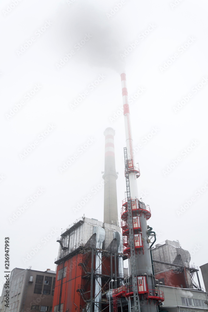 Old a new chimneys at heating plant covered in fog, cloudy winter day, low angle view, energy production, climate change and global, warming concept Old a new chimneys at heating plant covered in fog, cloudy winter day, low angle view, energy production, climate change and global, warming concept