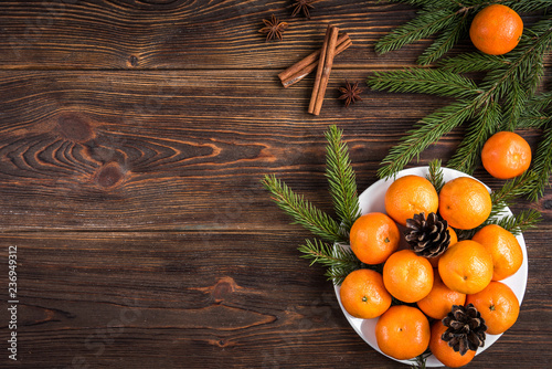 Fototapeta Naklejka Na Ścianę i Meble -  Mandarines on wooden background with Christmas fir branches, cinnamon sticks, anise stars and cones.