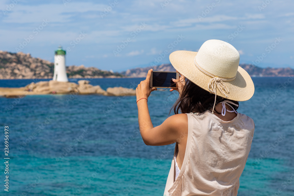 Young traveler woman making photo with mobile phone camera of lighthouse in Italy