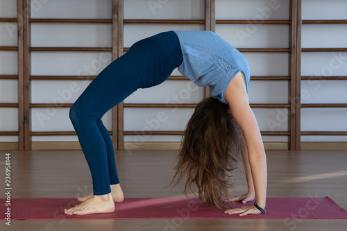 Beautiful photo of young lady standing in bridge exercise while practicing yoga poses on yoga mat