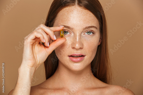 Beauty image of caucasian shirtless woman 20s holding vitamin pill, isolated over beige background photo