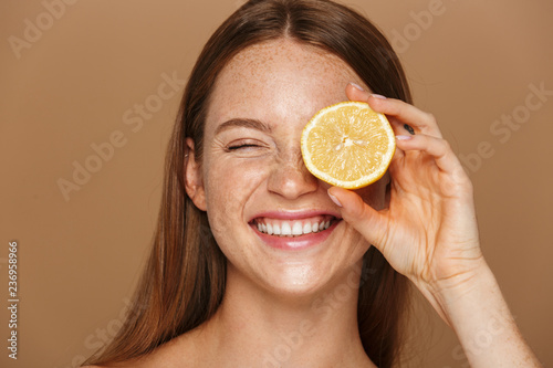 Beauty image of smiling shirtless woman with long hair holding piece of orange, isolated over beige background photo