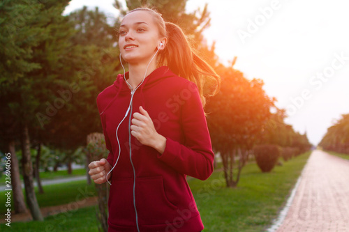 Fototapeta Naklejka Na Ścianę i Meble -  A young, fitness woman listening to music and running on the waterfront at sunset. Sports and healthy lifestyle.
