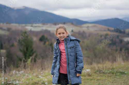  The child is smiling and happy against the backdrop of the mountains. Travel to the mountains. Girl happy in the mountains