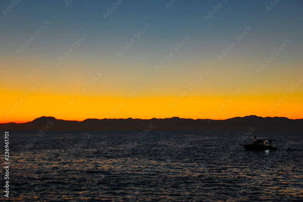 A small marine pleasure boat with tourists returns to port after sunset.
