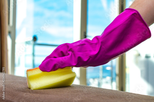 Housewife in rubber gloves is cleaning the house, wiping dust from the furniture with a rag and spray. Household chores photo