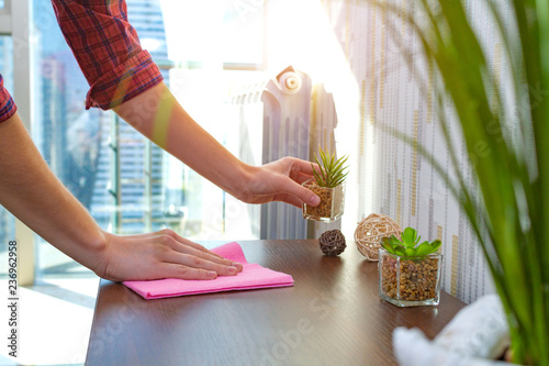 Canvas Print A housewife in a shirt is cleaning the house, wipes dust from the table with a cleaning rag