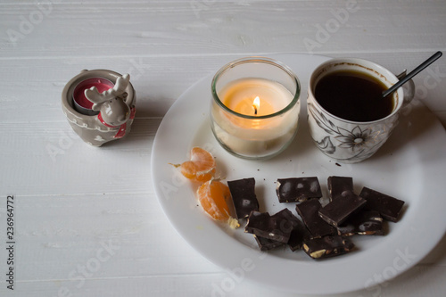 A candle, cup of coffee and black chocolate on the white plate.