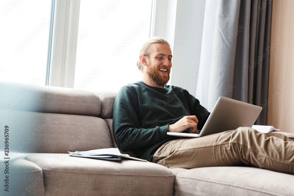 Concentrated young bearded man sitting in home using laptop computer.