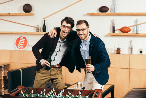 portrait of smiling businessmen with beer standing at table soccer in cafe