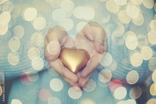 Woman hands are holding a beautiful glossy gold heart in a snow winter background. Love and St. Valentine cozy concept.