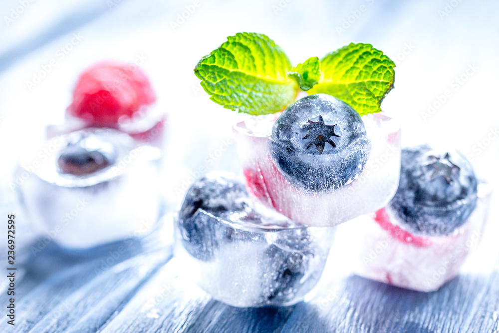 Berries frozen in ice cubes with mint on wooden table background - obrazy, fototapety, plakaty 