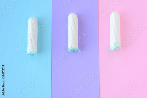 Three white tampons with selective focus and empty space on blurred colorful  pink  violet and blue background. Woman hygiene for period days  menstrual mothly cycle. Protective care for woman health.