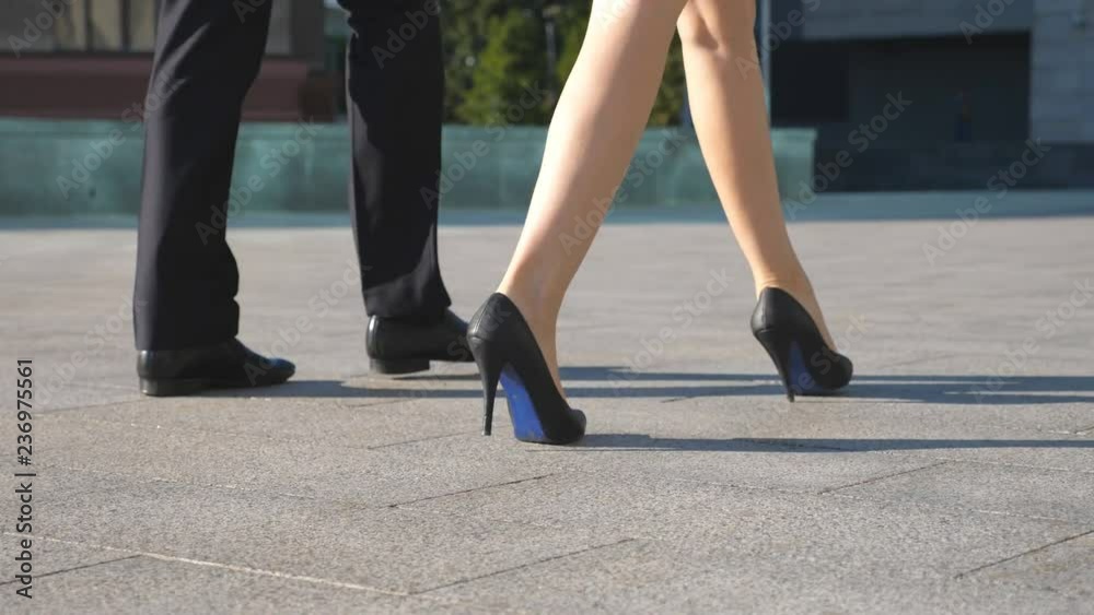 Feet of business man and woman in high heels shoes walking in urban street. Businessman and businesswoman commute to work together. Legs stepping to job. Colleagues going outdoor. Slow motion Close up Feet of business man and woman in high heels shoes walking in urban street. Businessman and businesswoman commute to work together. Legs stepping to job. Colleagues going outdoor. Slow motion Close up
