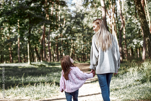 Happy little girl is walking with her beautiful mother in forest, rear view