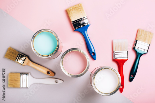 Fototapeta Naklejka Na Ścianę i Meble -  Three open cans of pastel paint with five brushes on pink and grey background. Renovation concept.