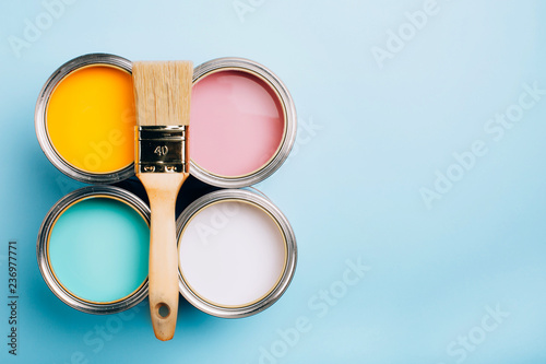 Brush with wooden handle on open cans on blue pastel background. Yellow, white, pink, turquoise colors. Renovation concept. Place for text. photo