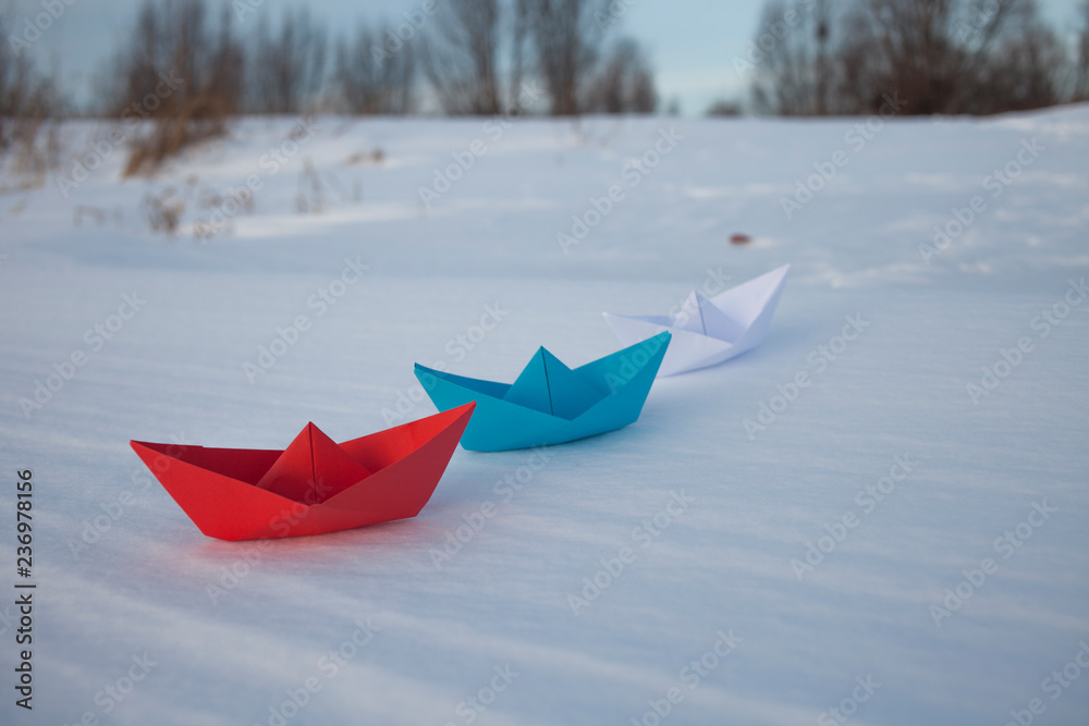 Red, blue and white paper boat in the snow.