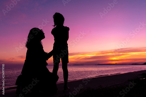Silhouette tourist family relaxing on beach in sunset, twilight sky