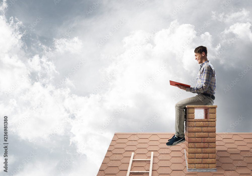 Handsome man on brick roof against cloud scape reading book Handsome man on brick roof against cloud scape reading book
