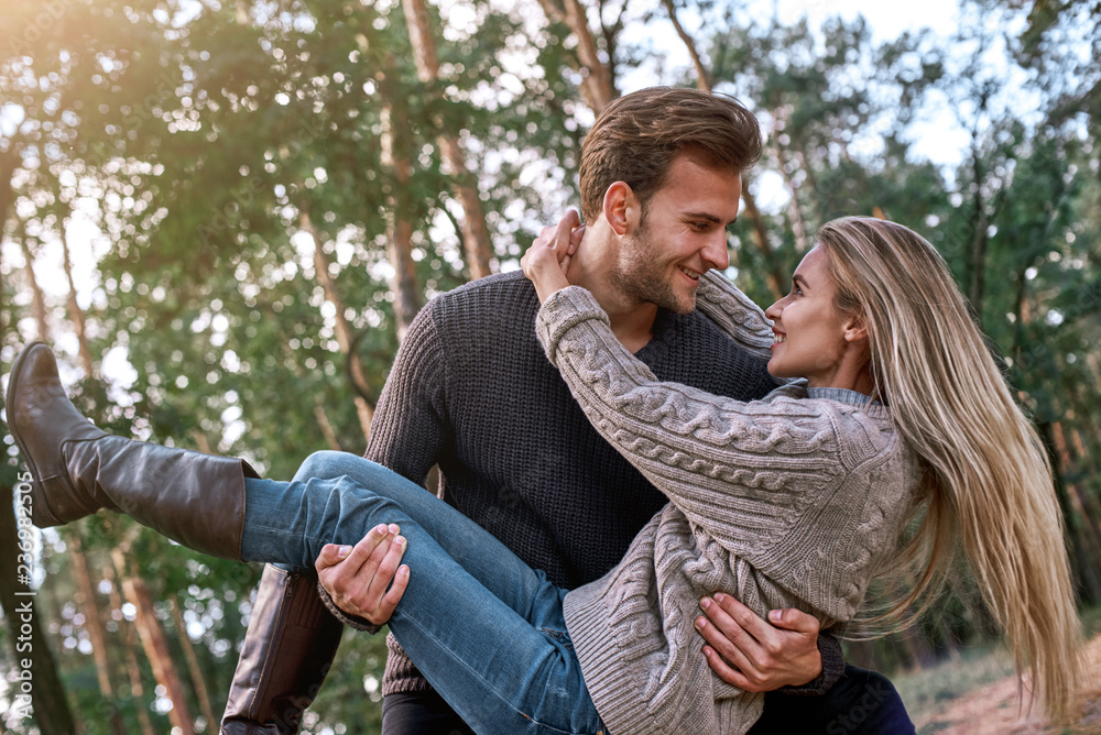 Fototapeta premium Young man holding his girlfriend on hands in autumn forest.
