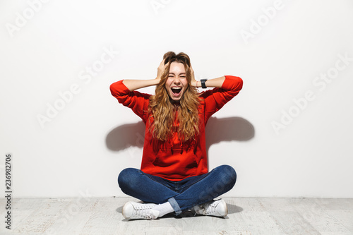 Full length photo of caucasian woman 20s wearing casual clothes smiling while sitting on floor with legs crossed, isolated over white background