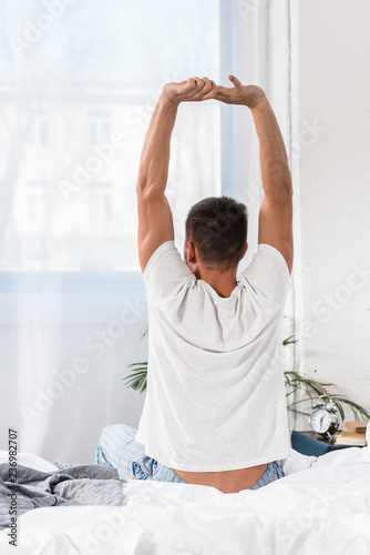 rear view of man stretching in morning in bedroom