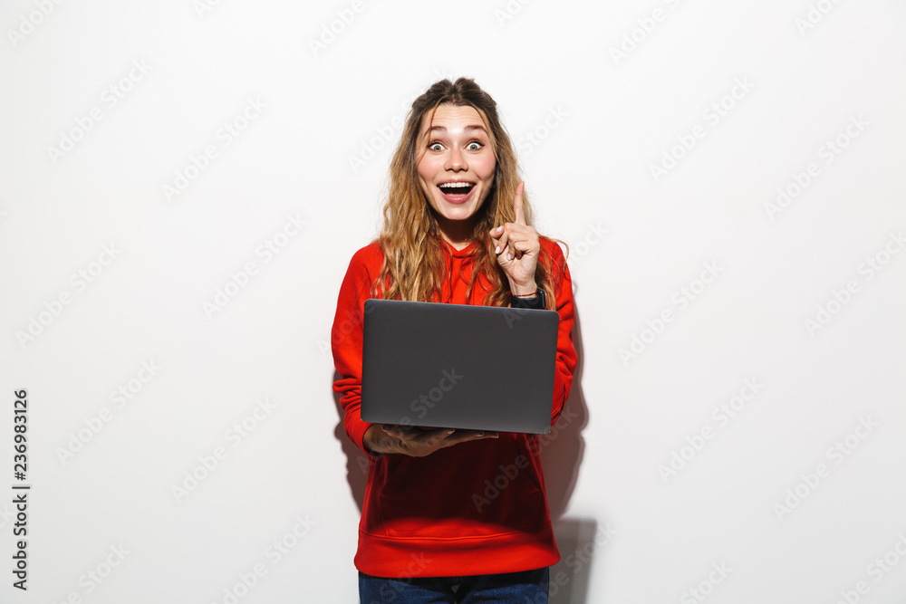Obraz premium Image of charming woman 20s wearing red sweatshirt holding laptop, isolated over white background