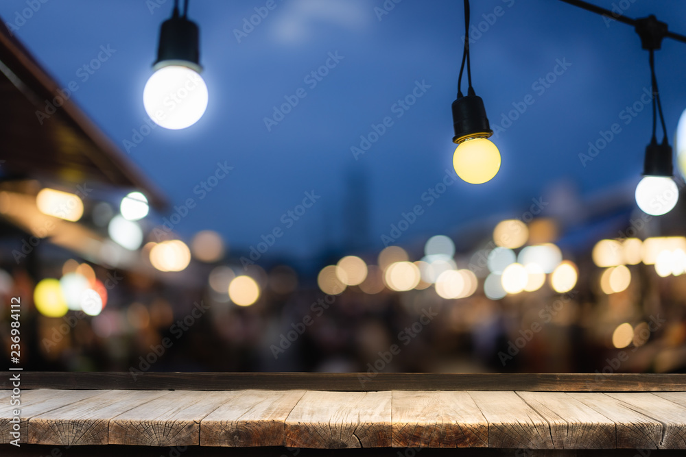 Wooden table in front of decorative outdoor string lights hanging on electricity post with blur people. Business, festival and holiday concepts, can used for display or montage your products. Wooden table in front of decorative outdoor string lights hanging on electricity post with blur people. Business, festival and holiday concepts, can used for display or montage your products.