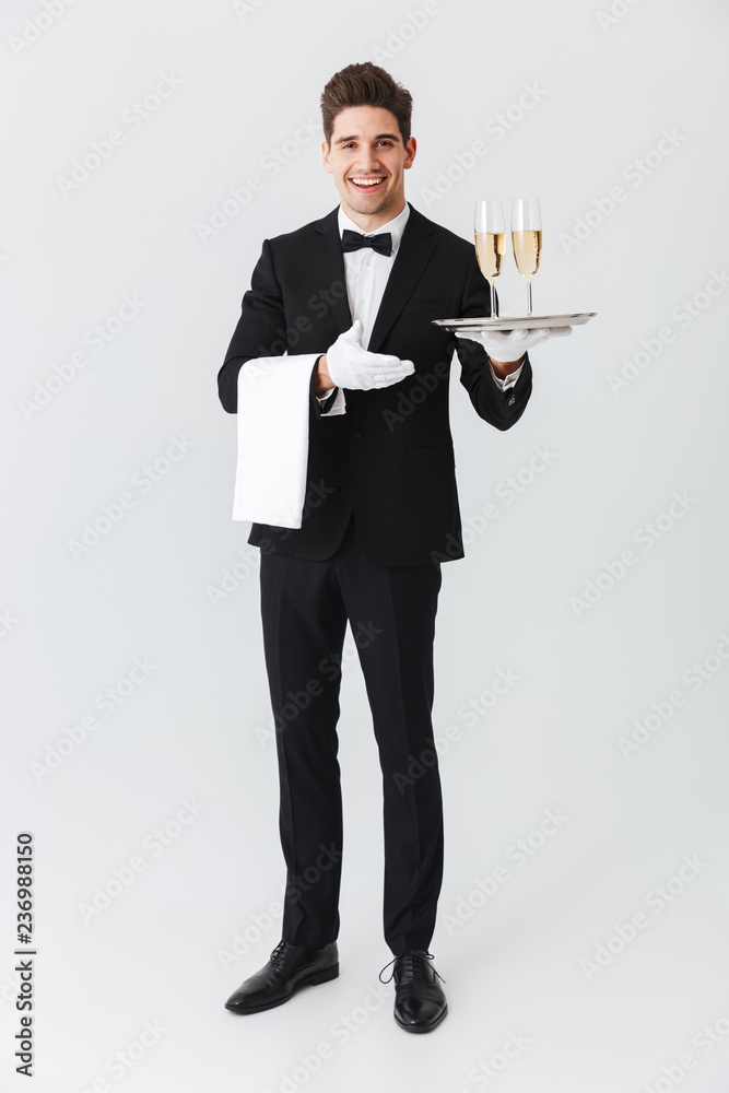 Full length portrait of a smiling young waiter in tuxedo Full length portrait of a smiling young waiter in tuxedo