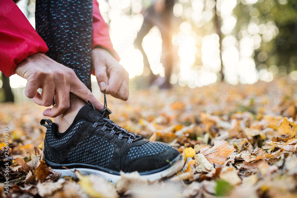 A midsection of female runner outdoors in autumn nature, tying shoelaces.