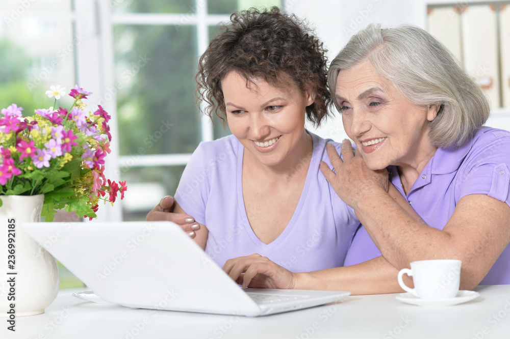 Portrait of cute senior woman with daughter using laptop