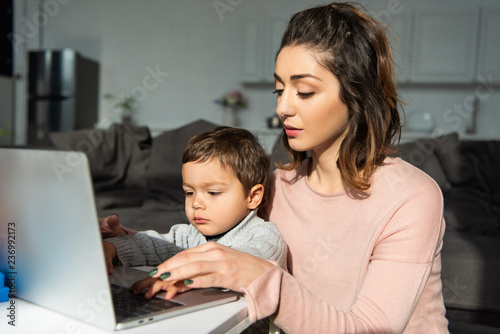 cute little boy and his mother using laptop at table in living room at home