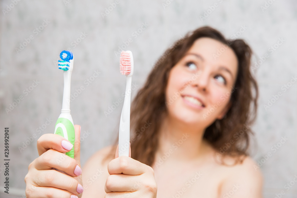 girl choosing an electric or ordinary toothbrush. Young woman holding toothbrushes in hands in the bathroom girl choosing an electric or ordinary toothbrush. Young woman holding toothbrushes in hands in the bathroom