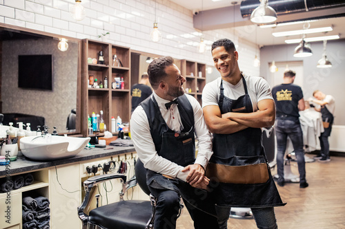 Two male haidressers and hairstylists sitting in barber shop.