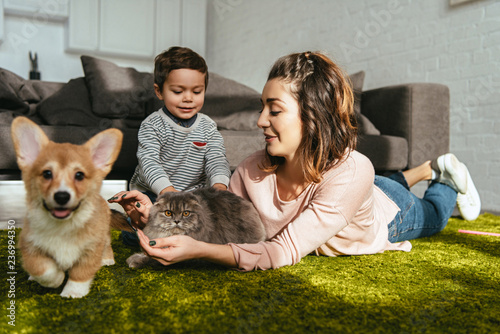 attractive woman and little boy laying on floor with dog and cat in living room at home