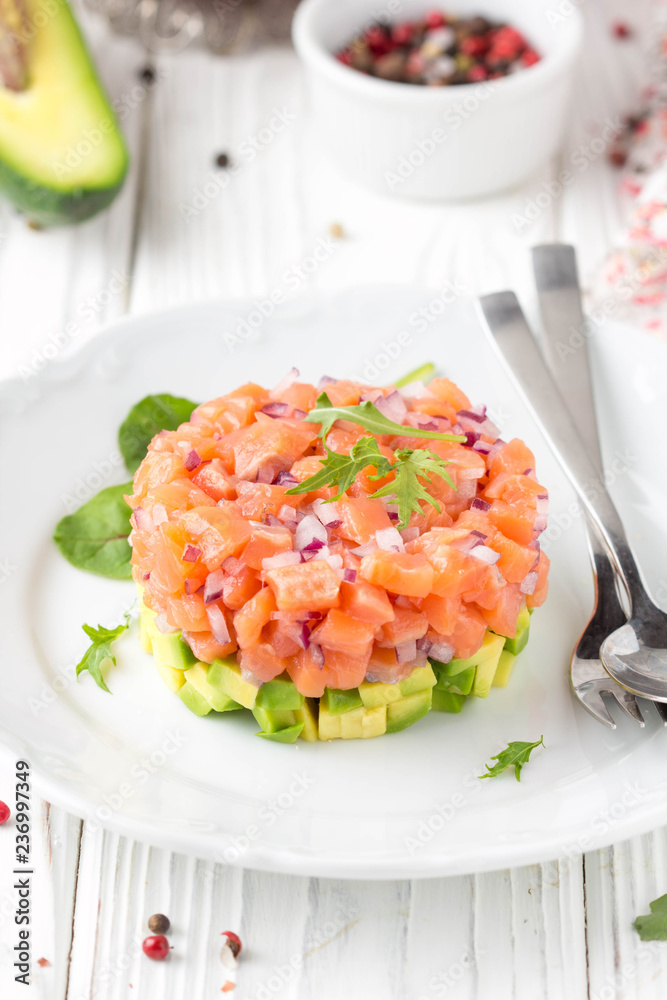 Salmon tartare with red onion, avocado, arugula, bread toast. Beautiful snack, dietary food, appetizer for Christmas holiday. On white wooden background Salmon tartare with red onion, avocado, arugula, bread toast. Beautiful snack, dietary food, appetizer for Christmas holiday. On white wooden background