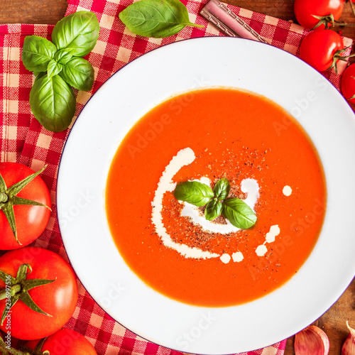 Tomato Soup composition with fresh tomatoes, basil leaf and garlic on a wood table, view from above. Vegetarian Autumn Food