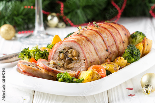Pork roll wrapped in bacon stuffed with mushrooms and beans, vegetables on the side. Beautiful festive main dish for Christmas holidays