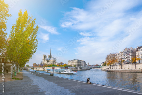 Cathedral of Notre Dame de Paris at sunny autumn afternoon. Embankment of the Seine. Boat on scenic route. Tourists a walk and relax in warm weather. Blurred unrecognizable faces. Paris. France.
