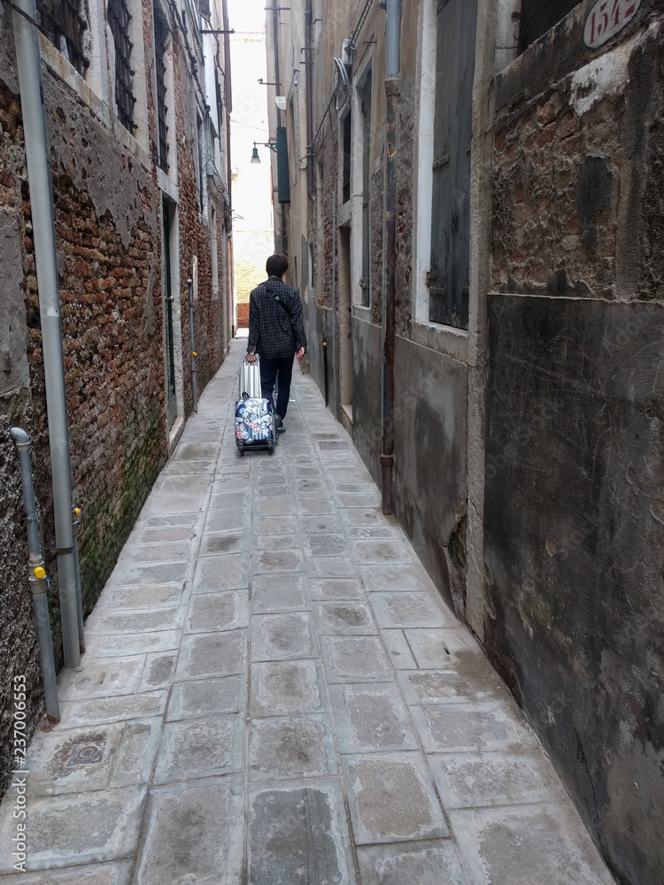 A tourist with luggage in a narrow street of Venice, Veneto, Italy. A tourist with luggage in a narrow street of Venice, Veneto, Italy.