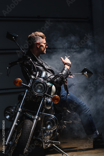 classic stylish rider in sunglasses leaning on motorcycle in garage