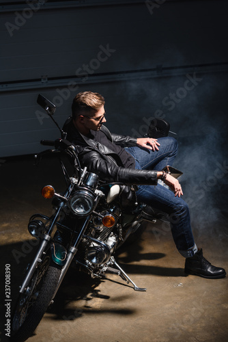 side view of handsome guy in sunglasses sitting on motorcycle in garage