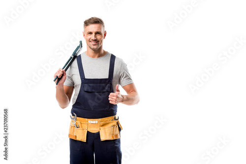smiling plumber holding pipe wrench and showing thumb up sign isolated on white