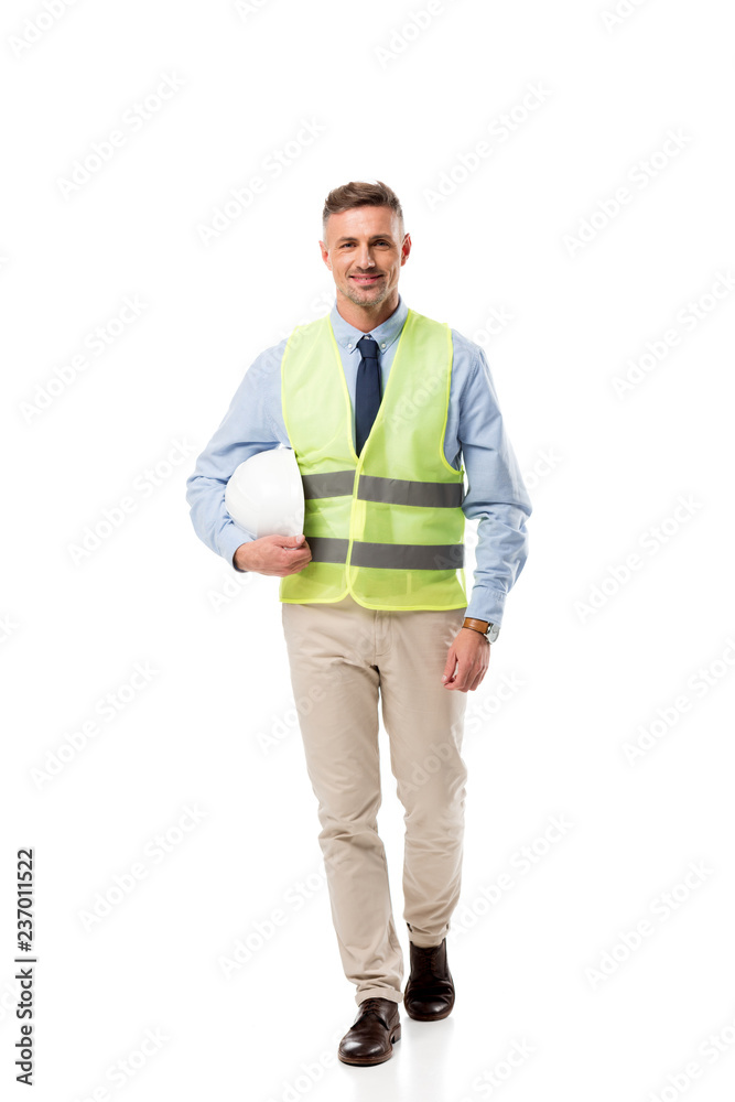 smiling engineer in safety vest holding helmet and looking at camera isolated on white smiling engineer in safety vest holding helmet and looking at camera isolated on white